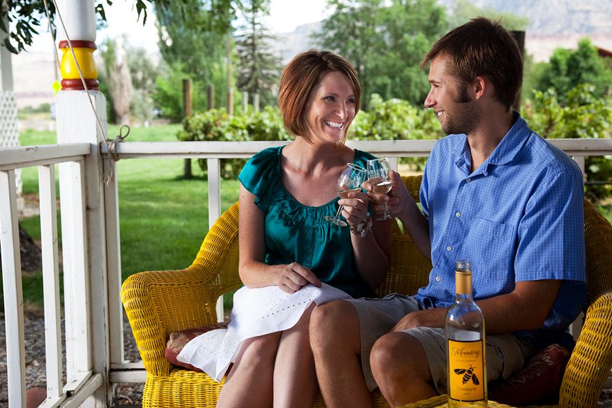 People enjoying drinks and conversation on a sunny porch with yellow pillows.