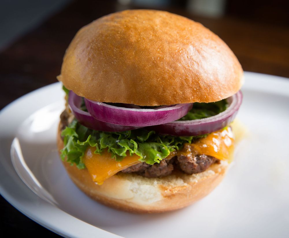 Classic cheeseburger with lettuce and red onion on white plate.