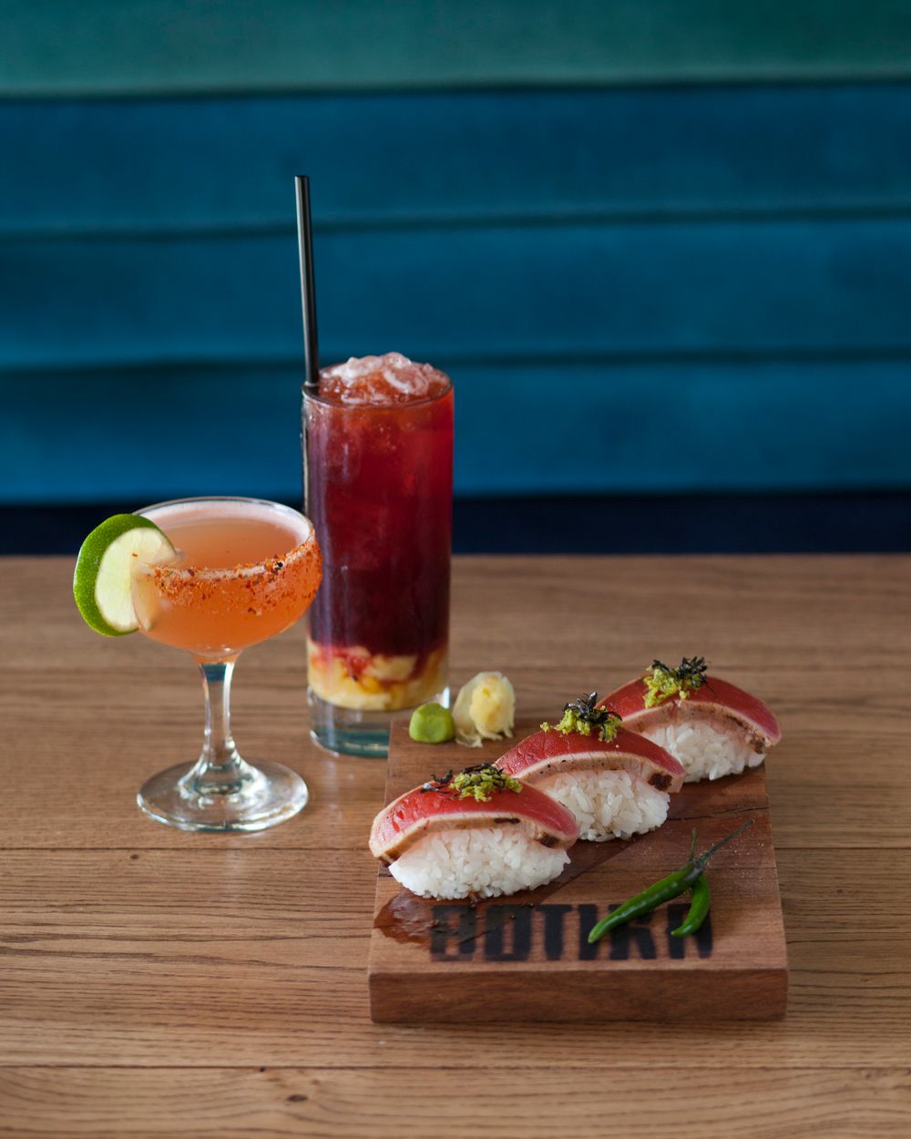 Elegant cocktails and sushi bites arranged on wooden serving board with garnishes.