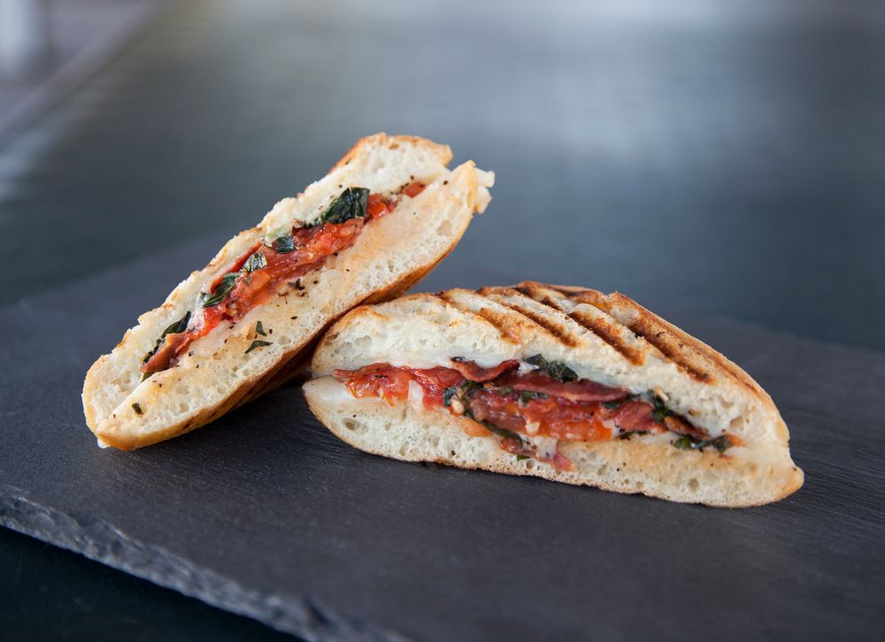Grilled panini sandwich filled with tomatoes, mozzarella and basil on black slate board.
