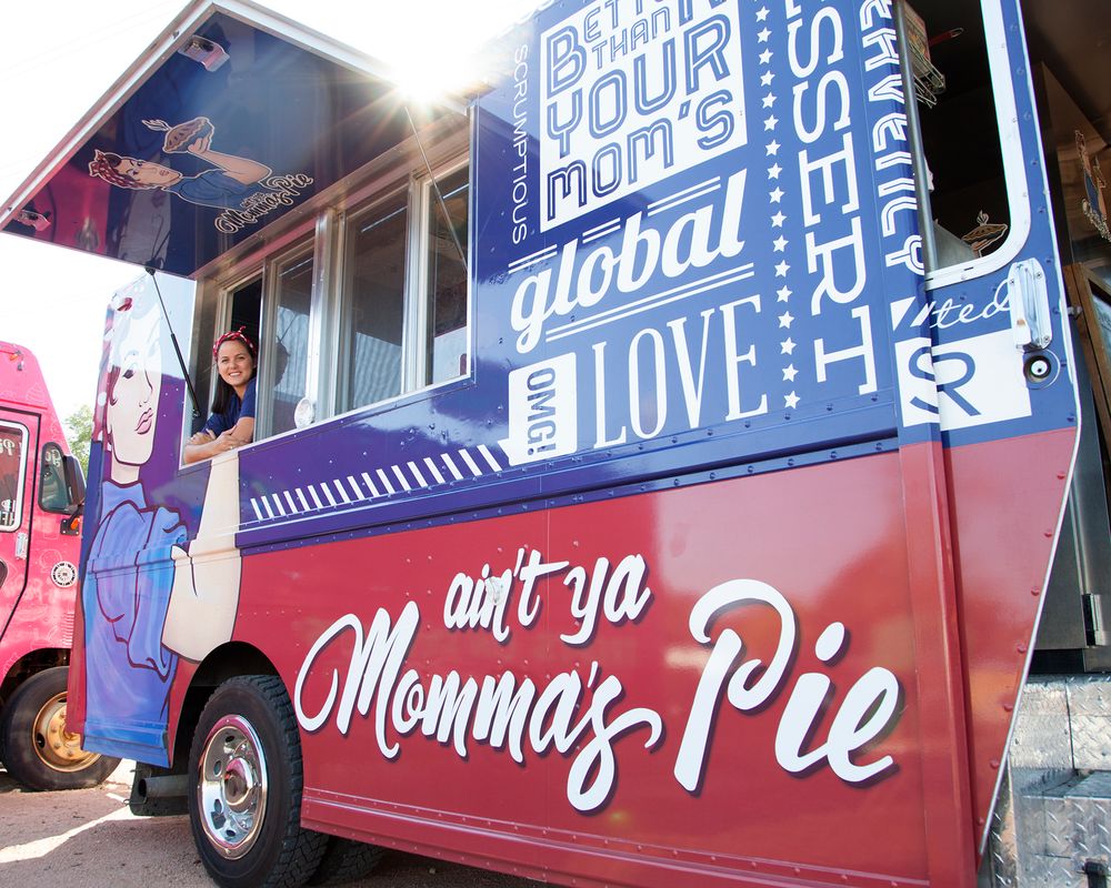 Blue and red food truck exterior with signage parked on street.