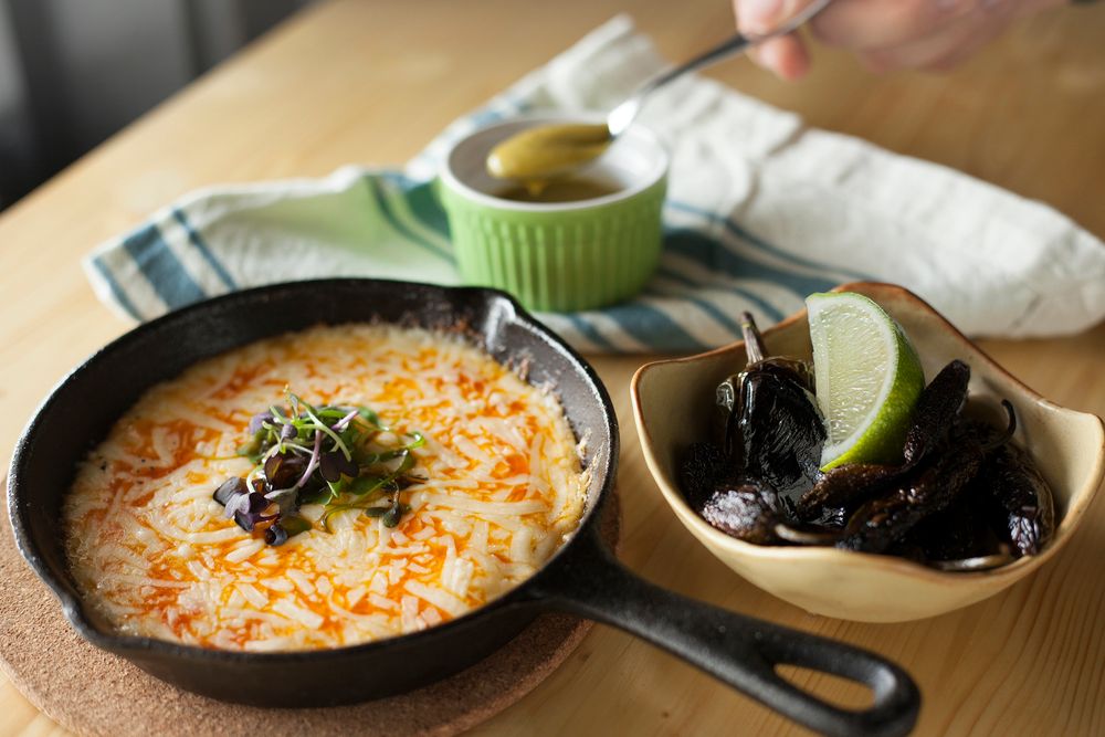 Closeup of melted cheese skillet dish with pickles and garnish on wooden table.
