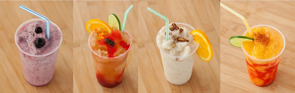 Colorful cocktails and beverages in various glasses lined up across a wooden surface.