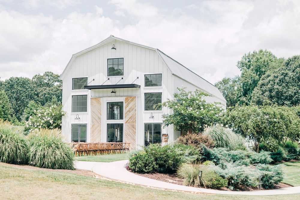 A modern white barn-style house with a rustic exterior and lush landscaping surrounded by green trees at the Barn South Wedding Venue