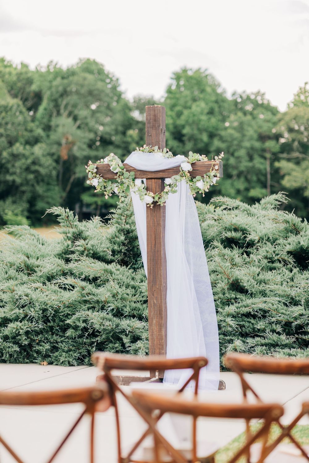 White fabric draping and floral arrangements adorn rustic wooden posts along an outdoor aisle setting.