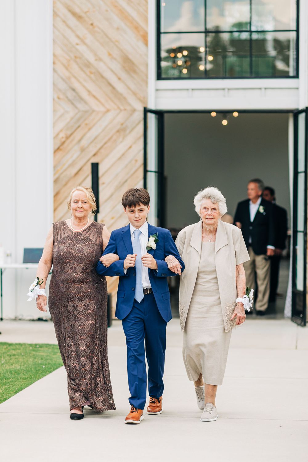 Three people walking at a modern venue entrance with diagonal wood paneling and glass windows.