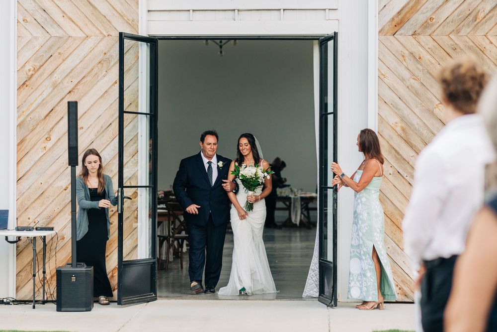 Two people dance together at a wedding reception in a modern white event space with geometric wood paneling behind them.