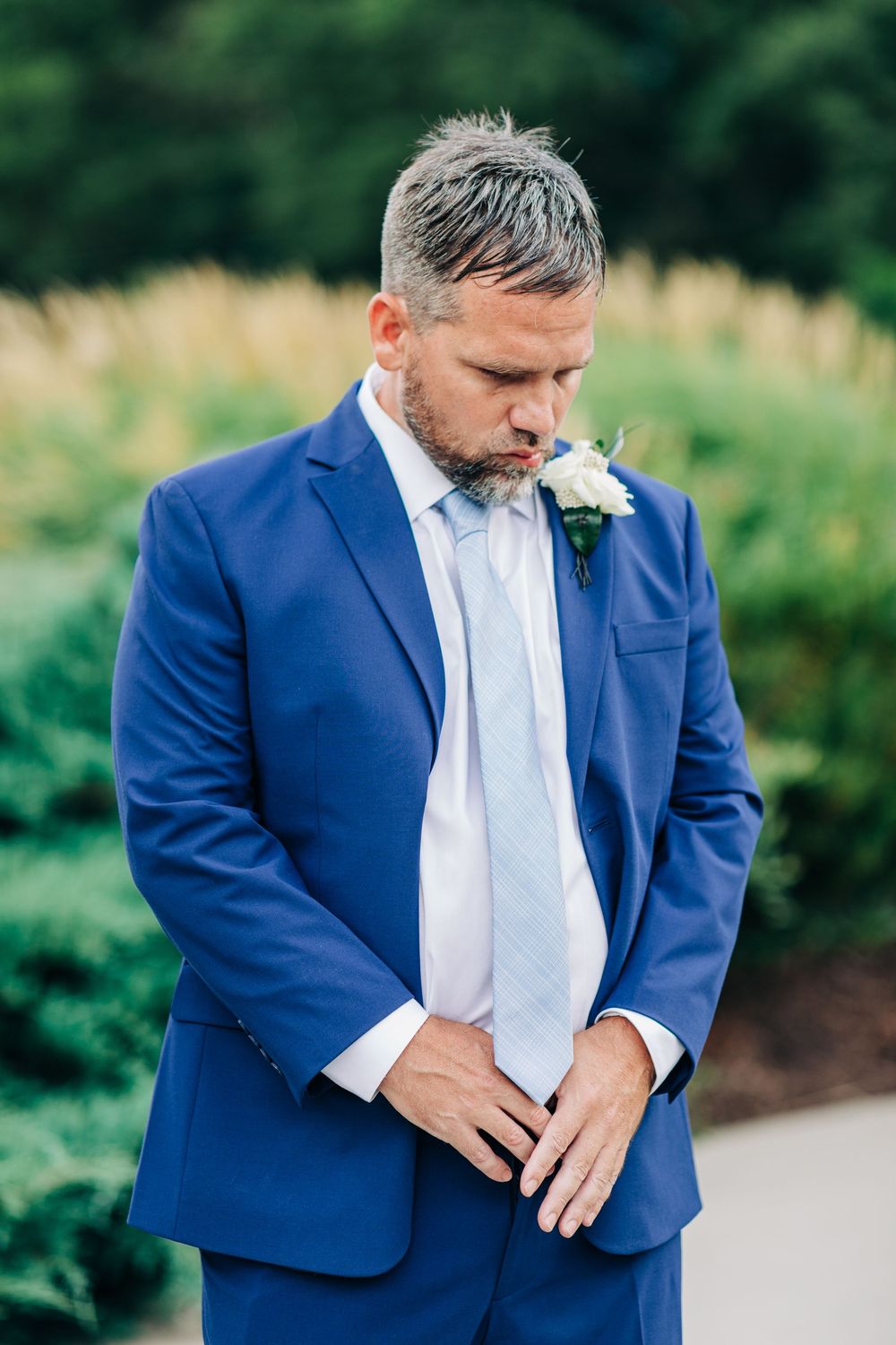 A groom in a navy blue suit and white tie adjusts his cuffs during an outdoor wedding photoshoot.