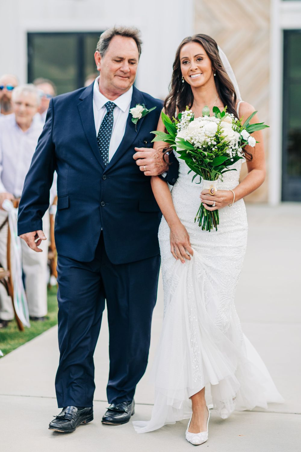 A formal wedding processional walking outdoors against a light colored building background.