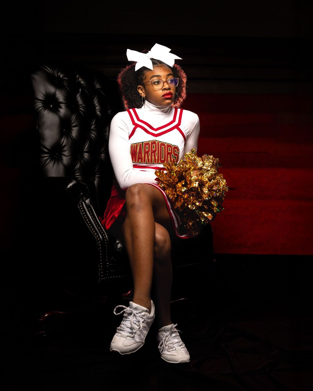 Low-angle shot of a cheerleader's uniform and pom poms against dark dramatic lighting.