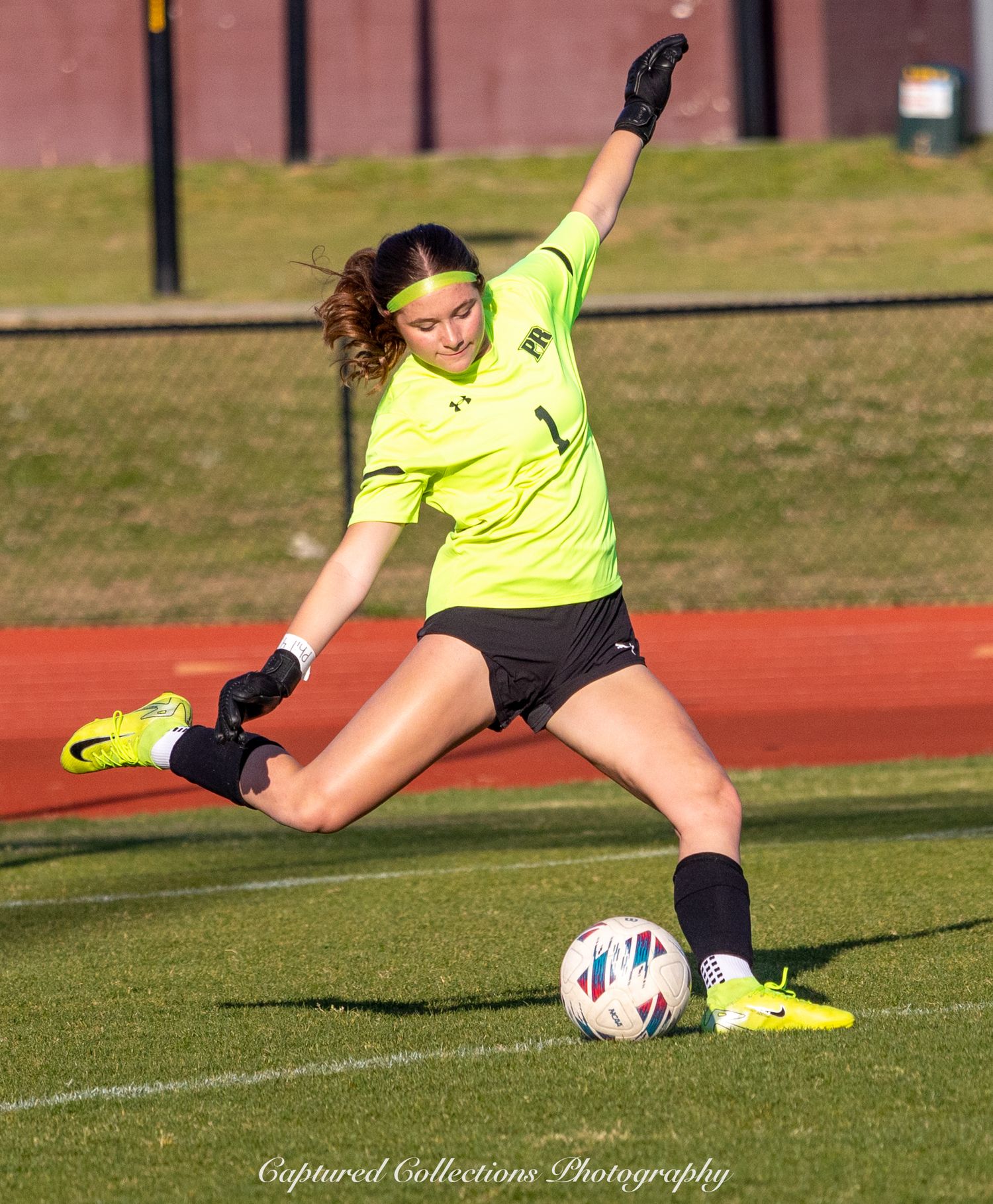 Soccer goalkeeper in bright yellow uniform makes a diving save on the field during daytime practice.