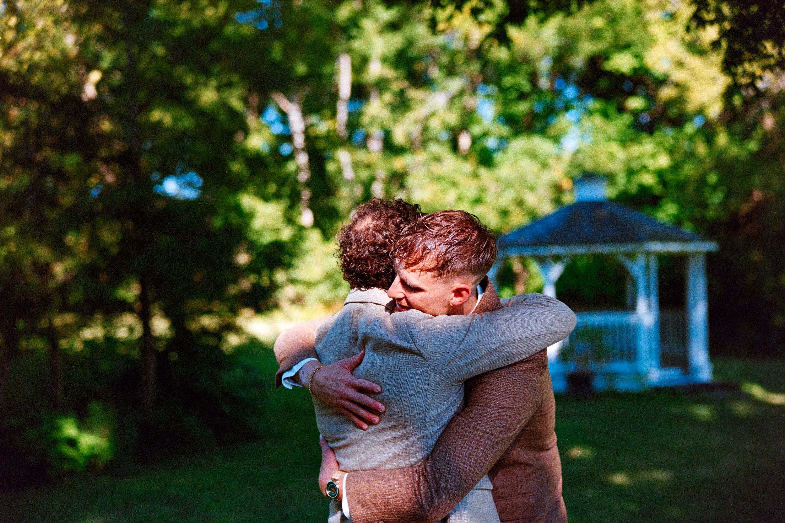 Group embraces each other in joyful hugs amidst a sunny outdoor setting with bright green foliage.