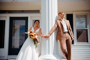Couple stands between white columns during wedding ceremony with bride in white dress holding autumn bouquet.