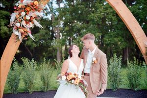Elegant wedding ceremony under a wooden arch decorated with autumn-colored flowers in an outdoor garden setting.