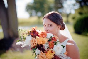 Bride with autumn-colored bouquet featuring orange and burgundy flowers in an outdoor garden setting.