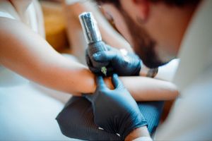 Close-up shot of a tattoo artist wearing black gloves working with a tattoo machine.
