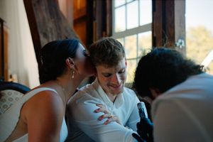 Wedding guests gathered in an indoor reception venue with natural light streaming through windows.