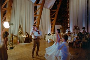 A couple dances together during their wedding reception in a rustic wooden venue with white drapes and soft lighting.