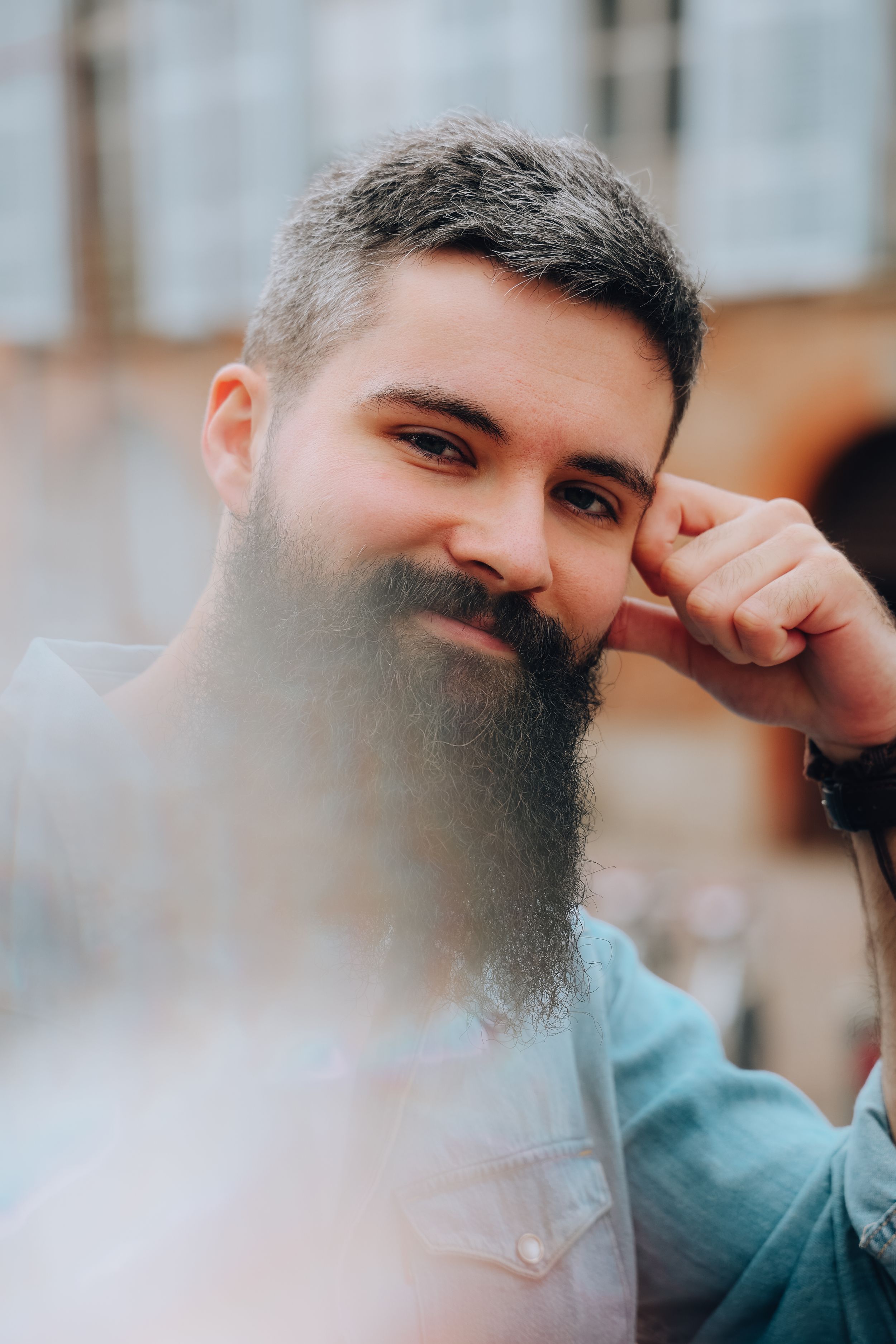 A close-up portrait of a bearded man with a thoughtful expression in an urban outdoor setting.