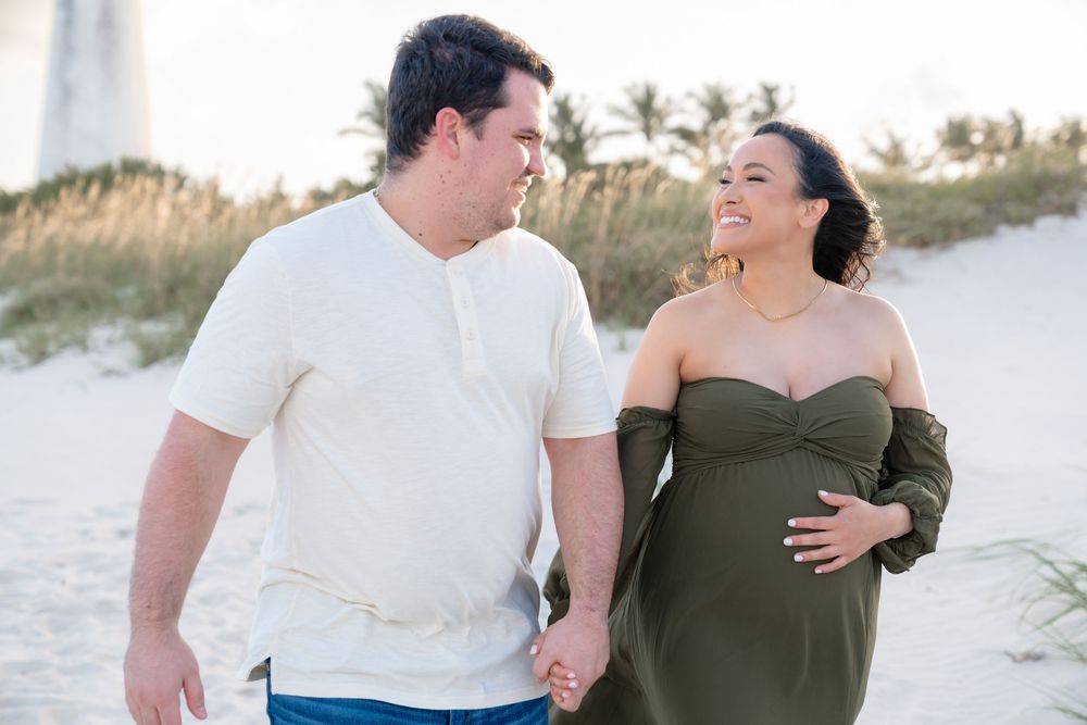 Couple in white and olive green attire sharing joyful moments during sunset beach photography session.