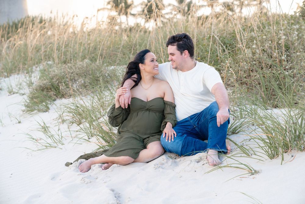 A romantic couple rests together on white sand dunes at the beach during golden hour.