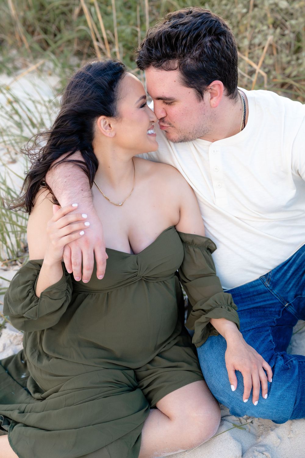 Intimate moment captured between couple on beach with woman in olive green dress.