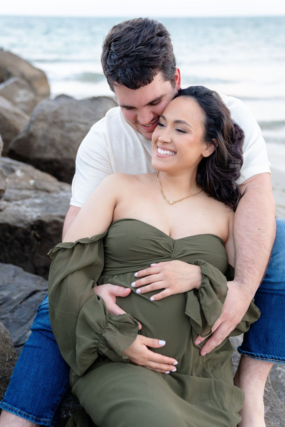 A couple shares intimate moments on a rocky beach during a romantic photoshoot.