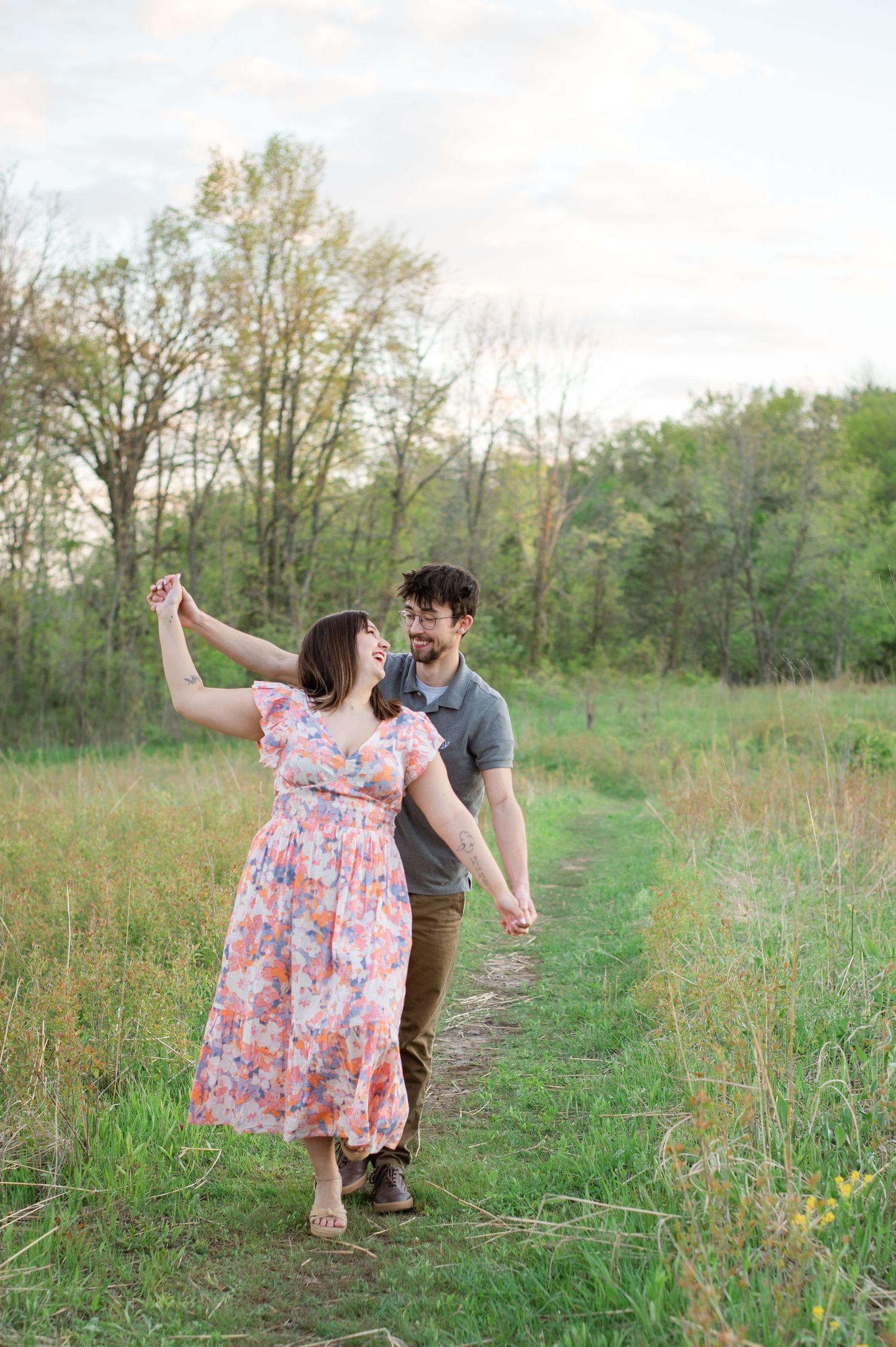 A couple dances together on a grassy path surrounded by wildflowers and trees on a spring afternoon.