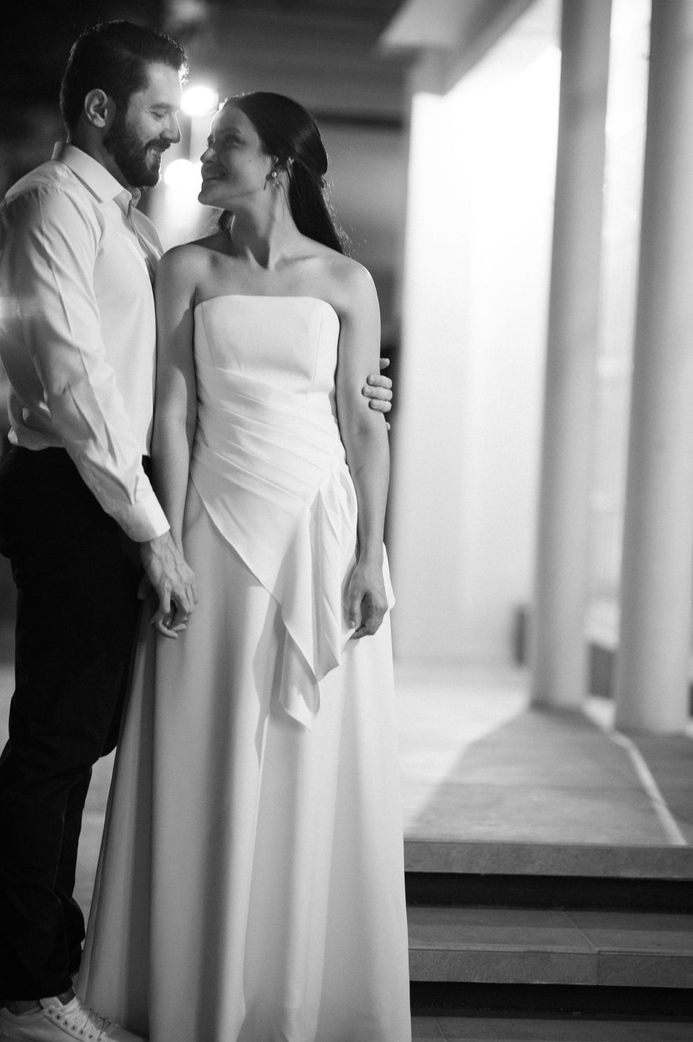 A romantic black and white portrait of a couple in wedding attire standing in a hallway.