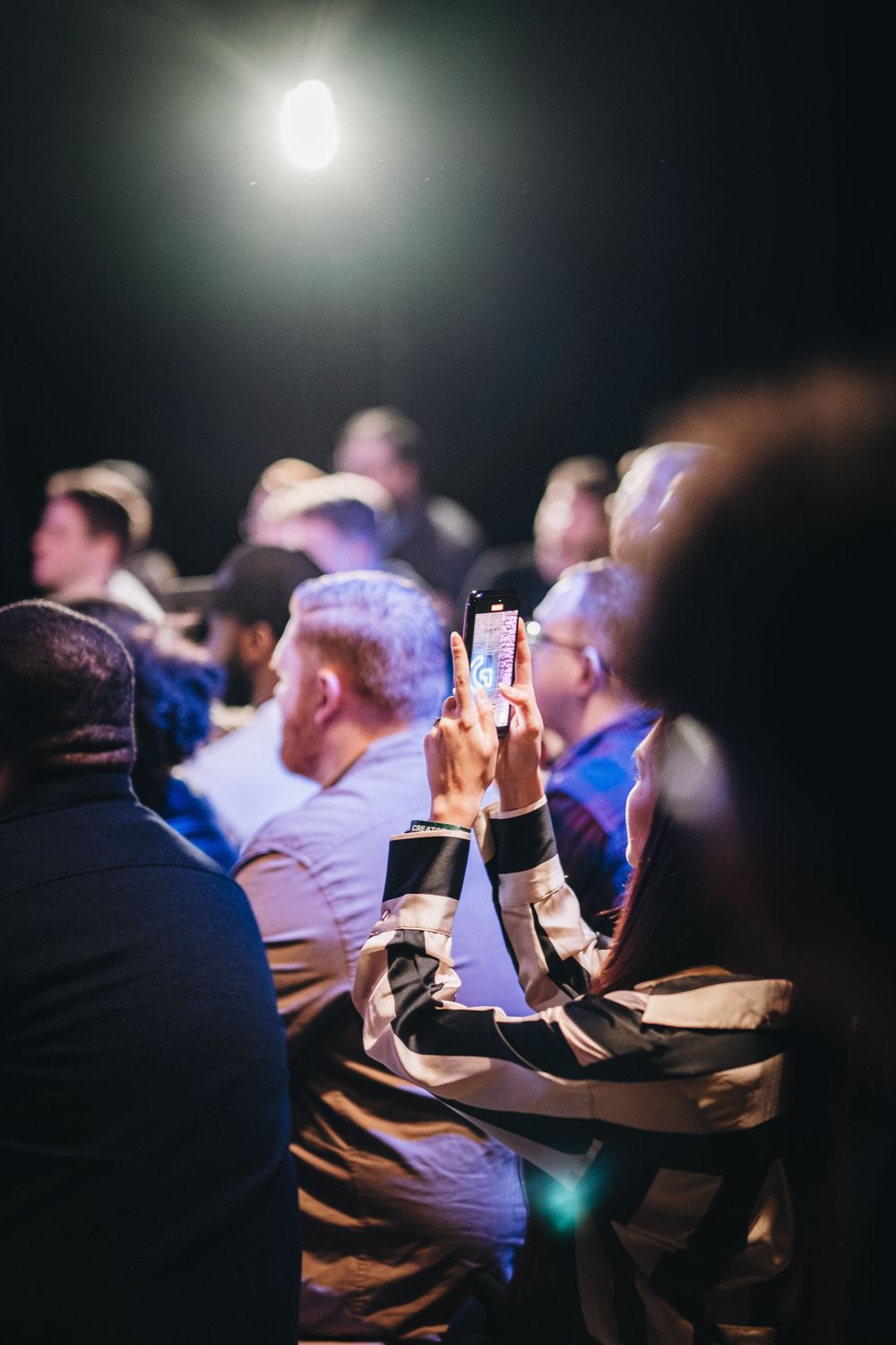 Audience members using mobile phones during a darkened conference presentation.