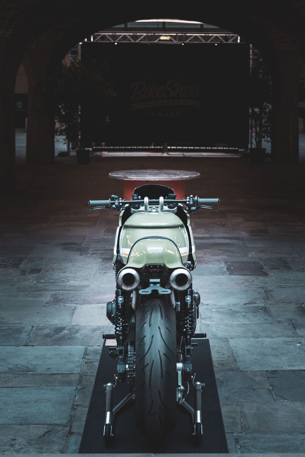 Dramatic lighting illuminates a custom motorcycle in a dark warehouse setting.