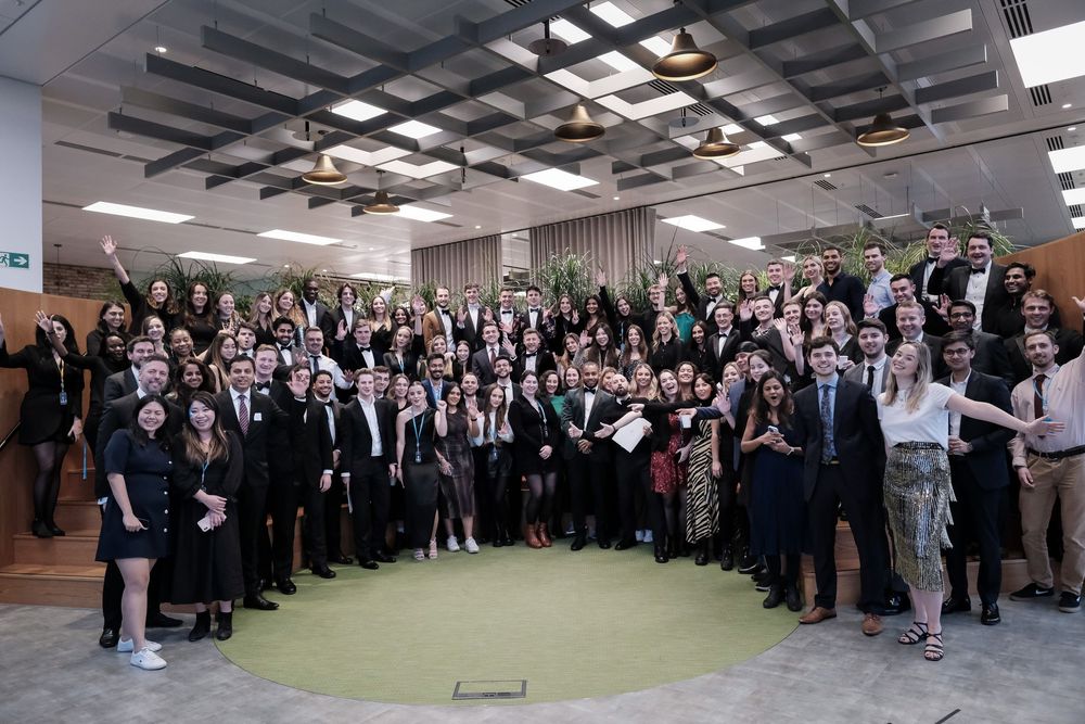 Large group of professionals in formal attire posing together in a modern office space for a group photo.