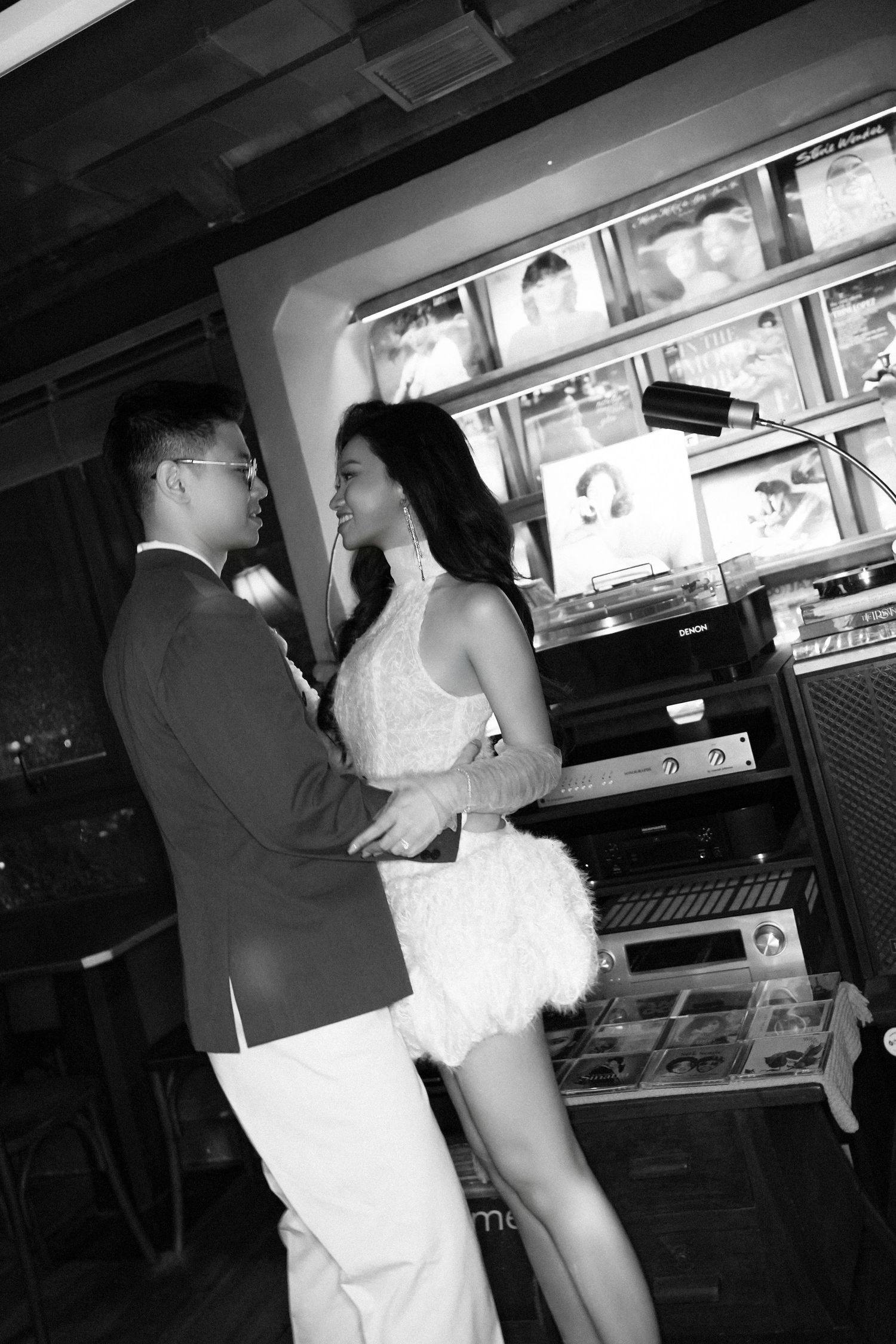 Black and white photo of a couple embracing near a vintage record player and music equipment.