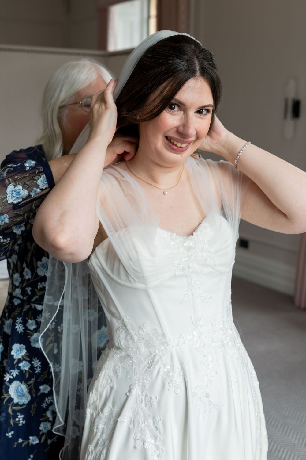 A bride in a classic white wedding dress has her veil adjusted while getting ready.
