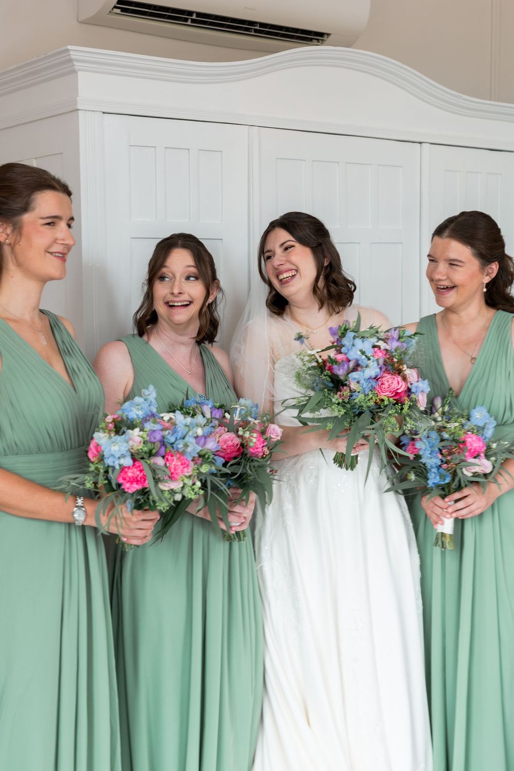 Bridesmaids in mint green dresses hold colorful bouquets while posing with the bride.