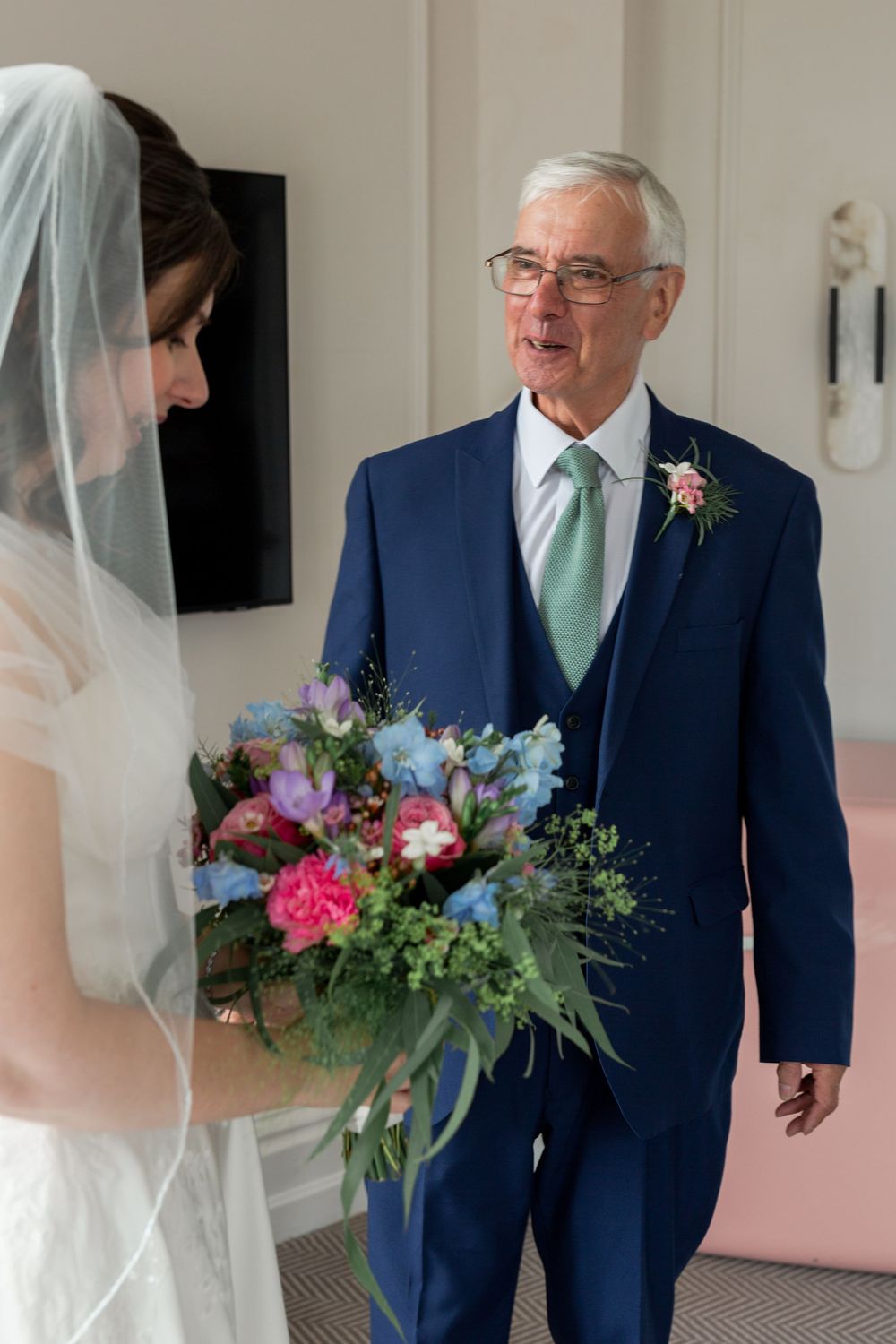 A touching moment between a bride with her bouquet and a gentleman in a navy suit with mint tie.