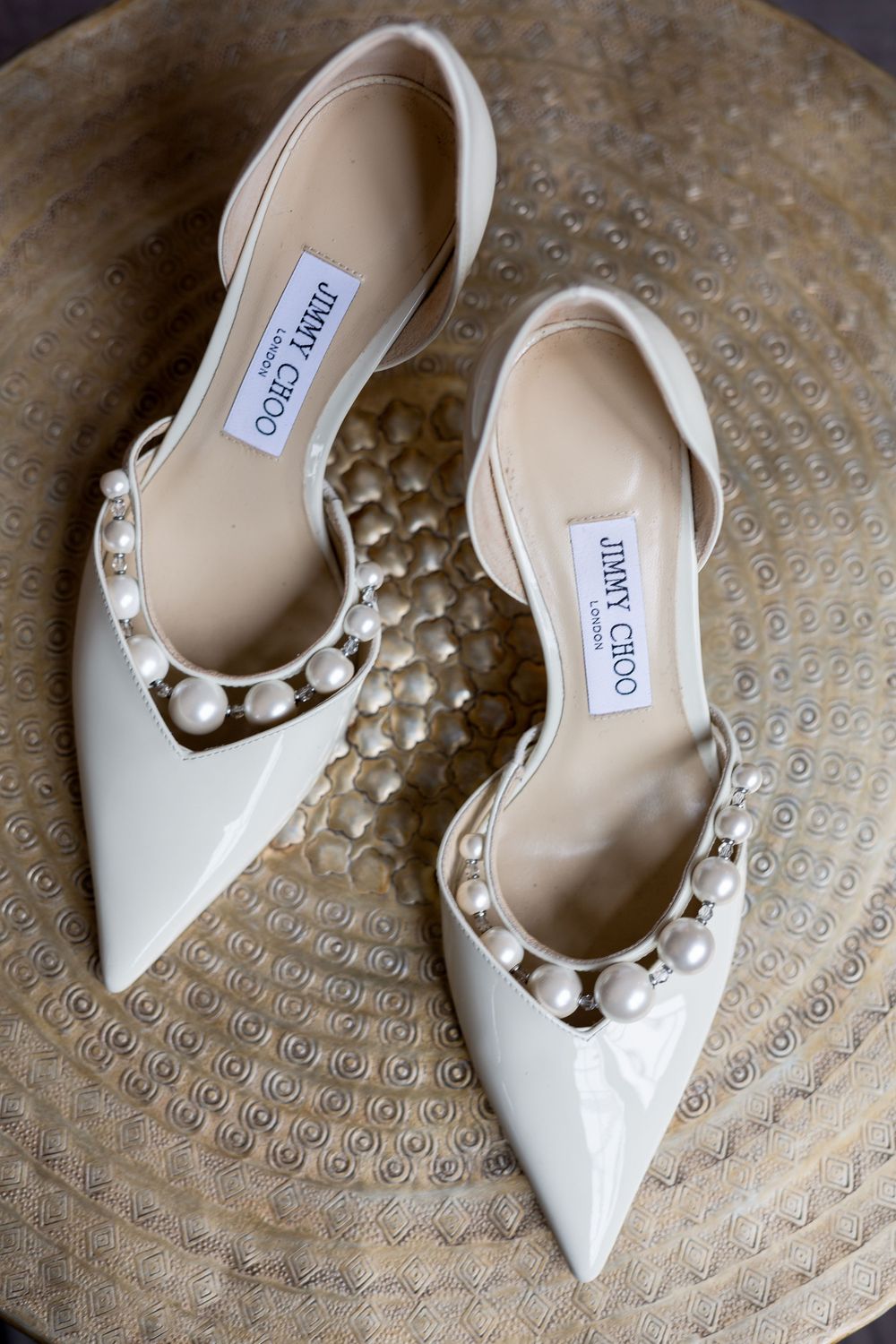 White bridal shoes with pearl details photographed on a textured metallic surface.