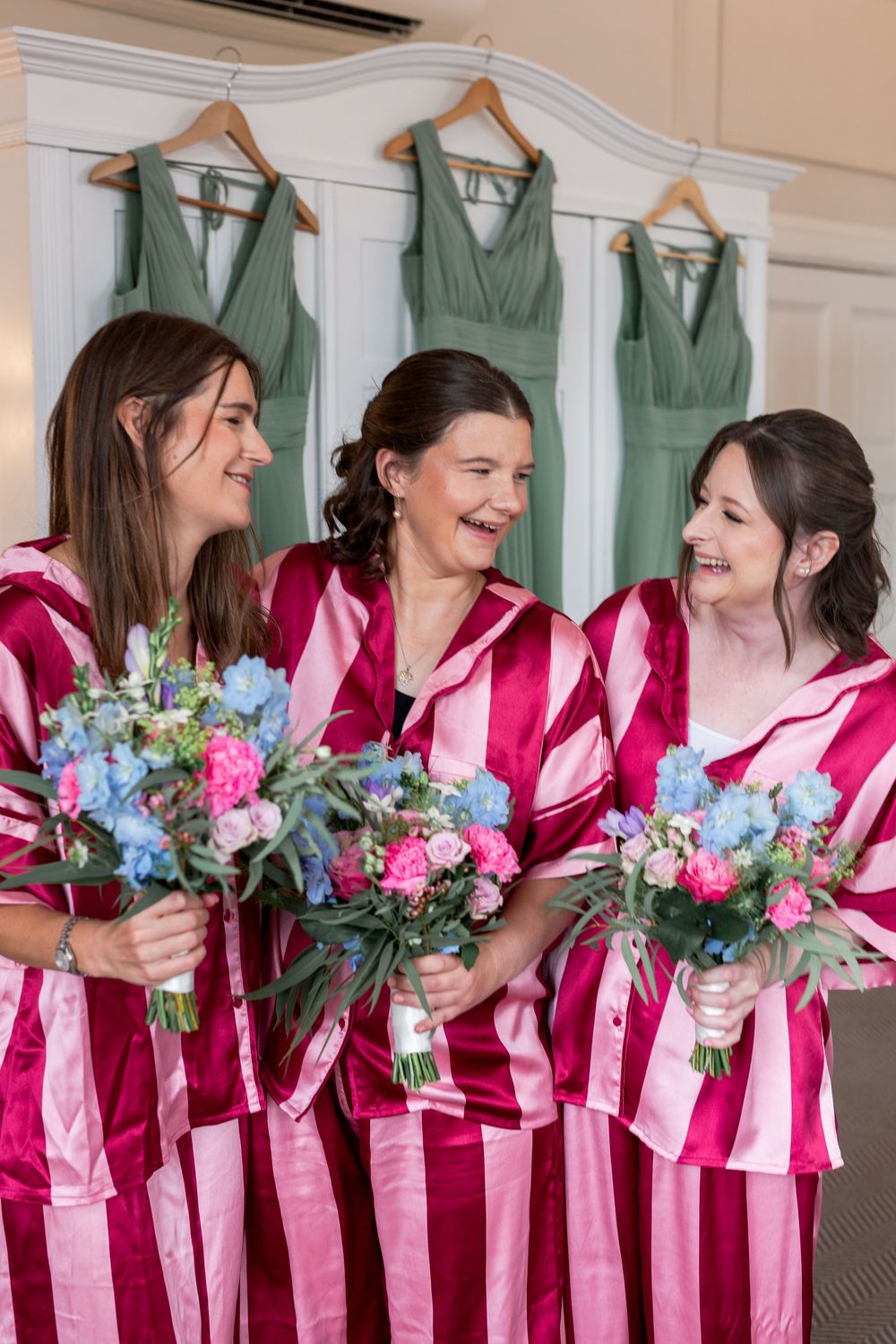 Bridesmaids in pink striped robes holding vibrant floral bouquets.