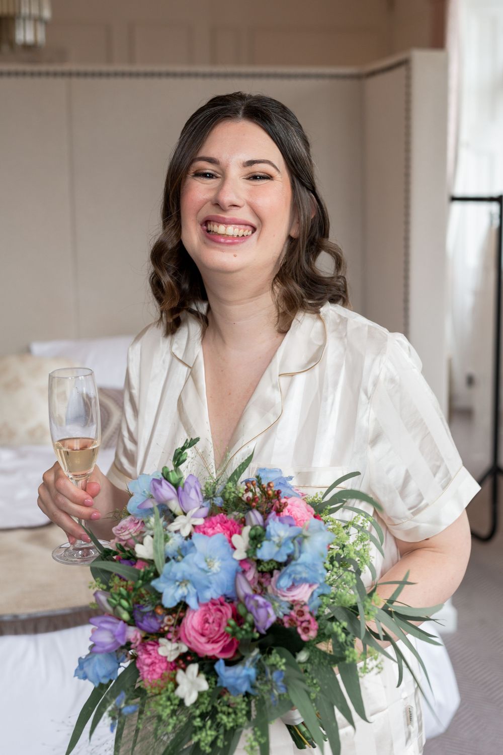 Colorful bridal bouquet with pink and blue flowers held against a white robe.