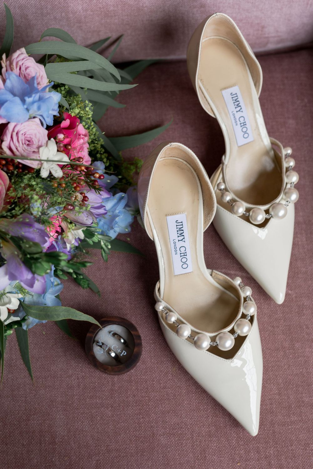 Elegant white bridal shoes with pearl accents displayed next to floral arrangements.