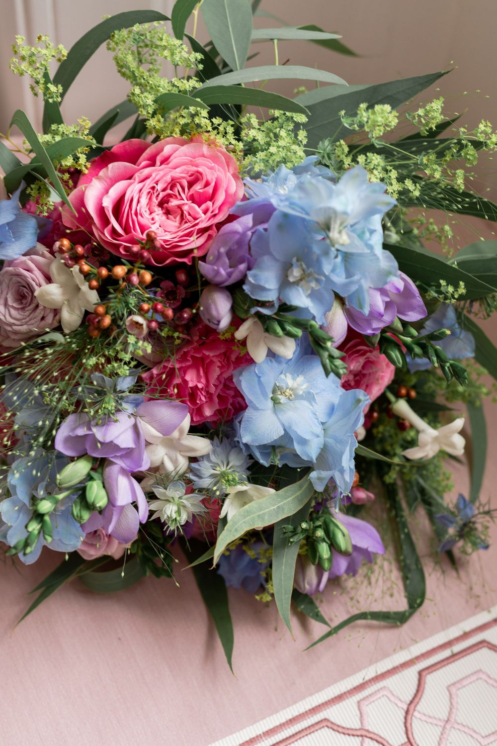 Lush floral arrangement featuring pink roses, blue hydrangeas, and greenery against a pink background.