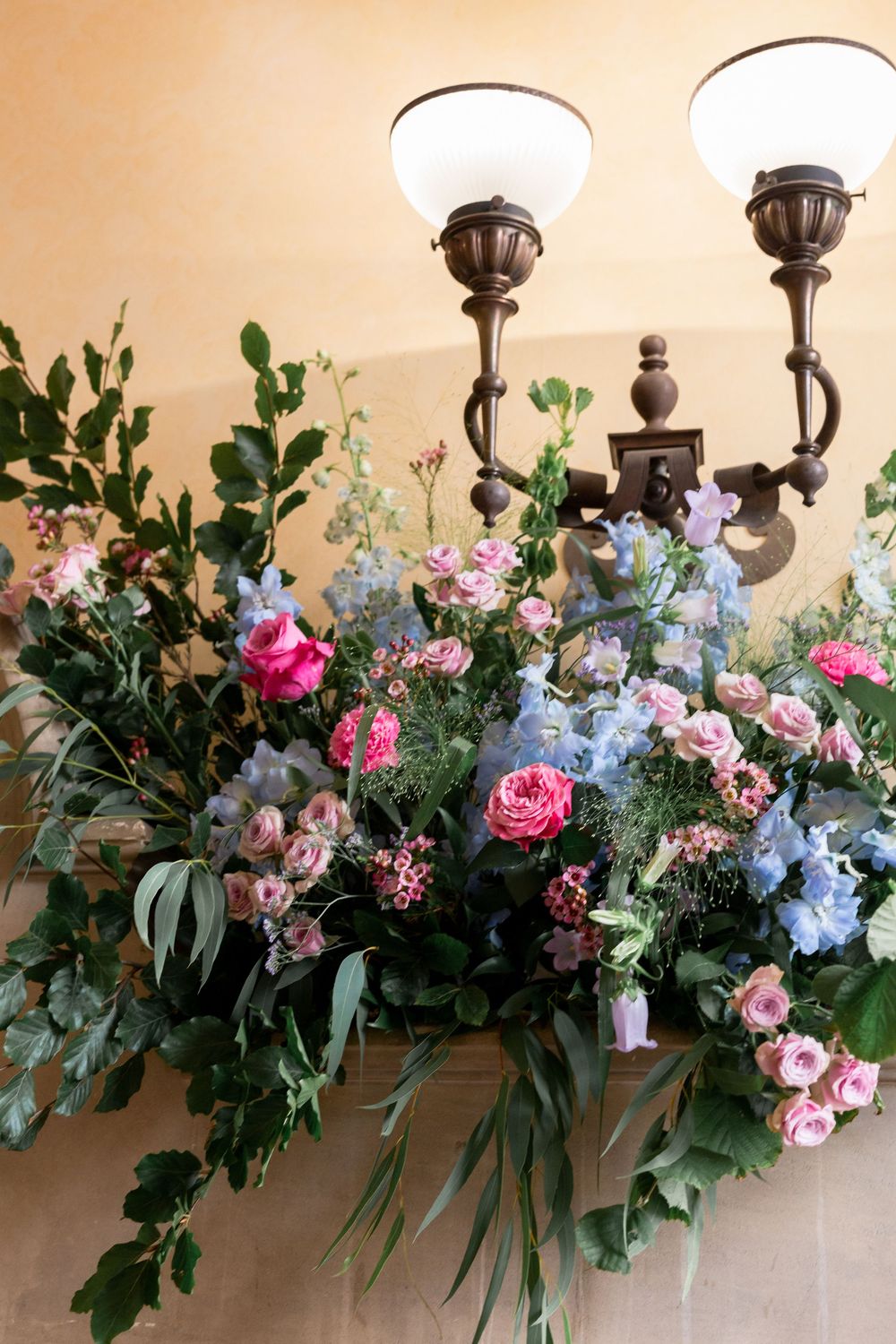 Romantic floral arrangement with pink roses and blue flowers against vintage wall sconces.