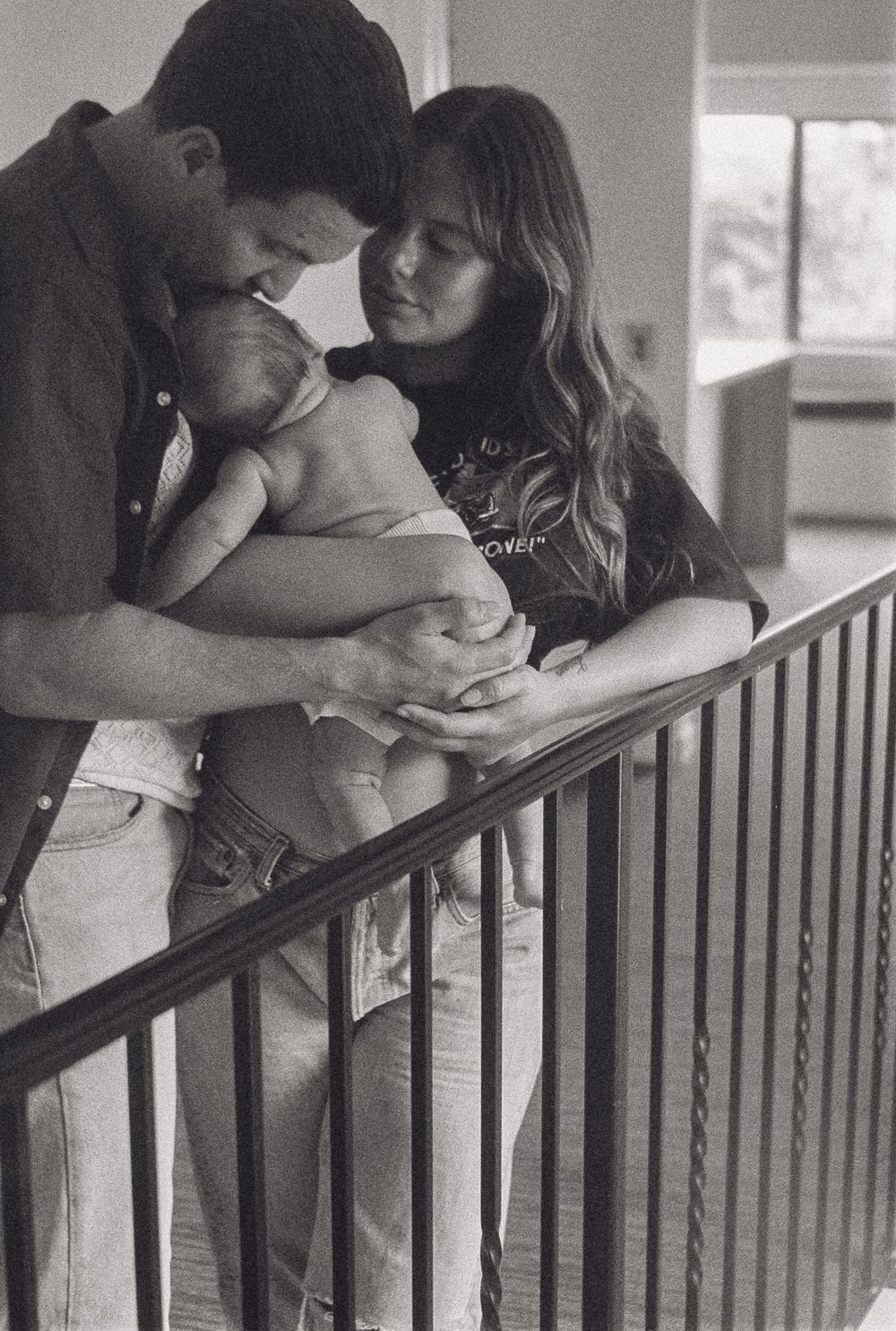 A tender black and white intimate family moment captured with a sleeping baby on a stairwell.