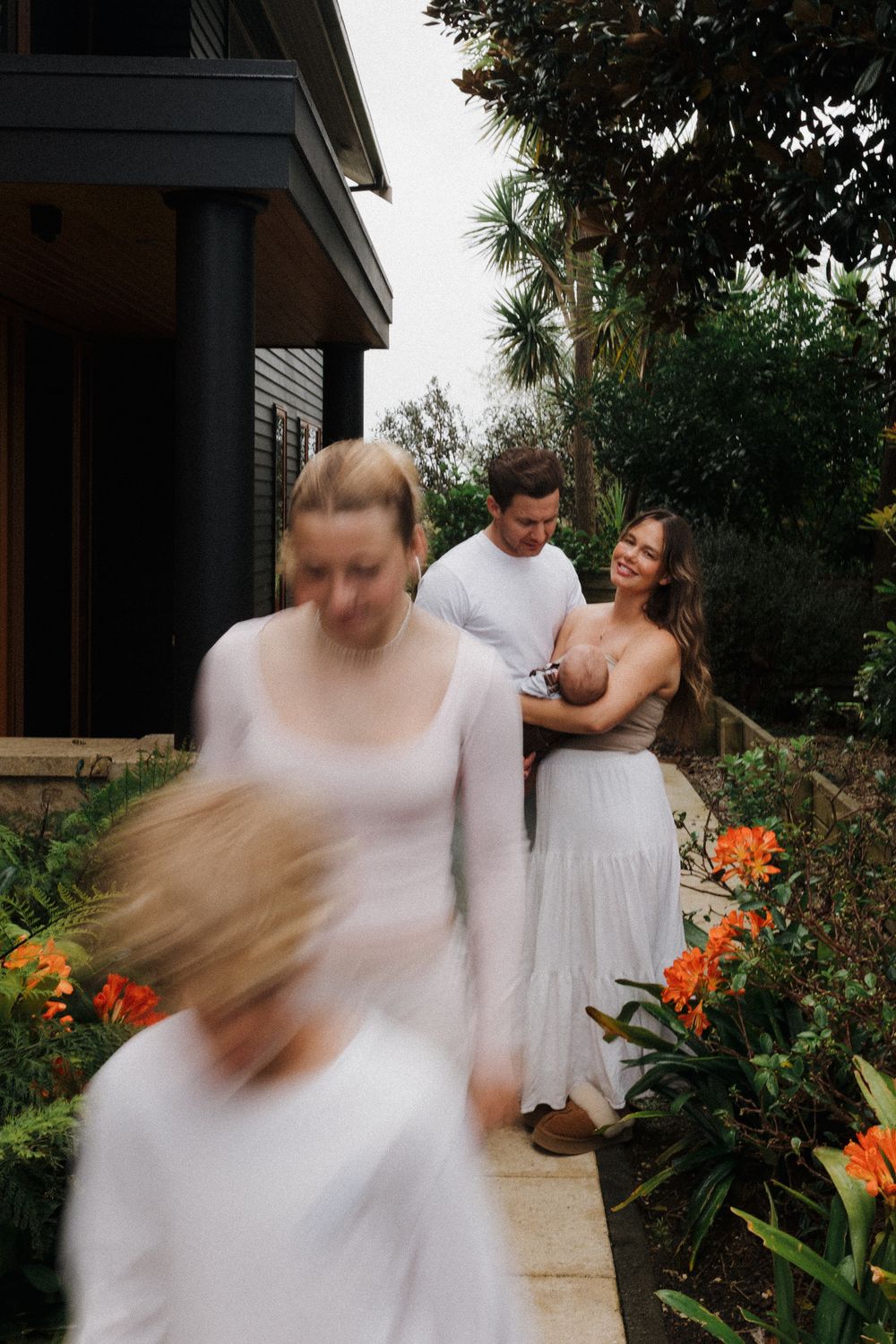 Motion-blurred dancing figures in white against a backdrop of orange flowers and greenery.