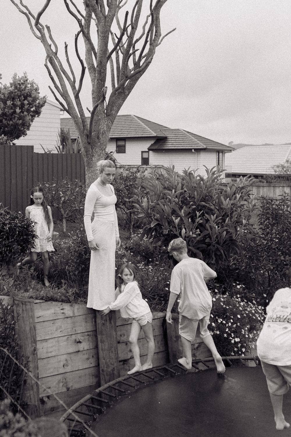 Children playing and climbing on wooden garden boxes in a backyard.