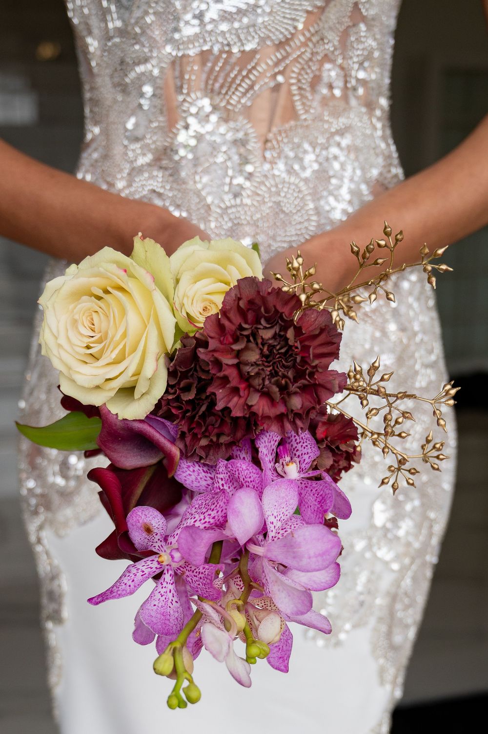 Close-up shots of wedding bouquet featuring cream roses, burgundy flowers and purple orchids against a white dress.