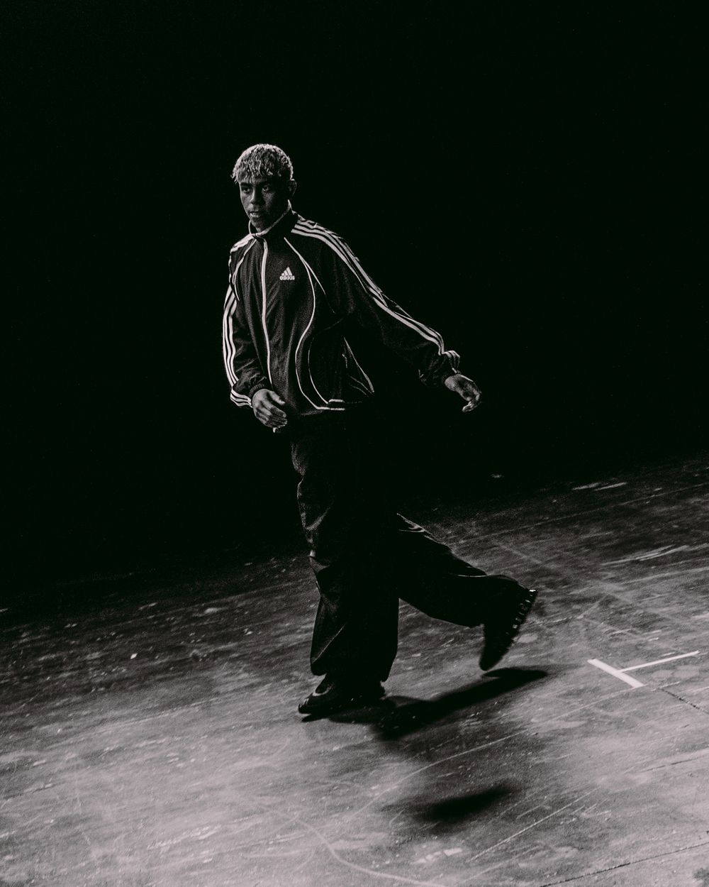 A series of black and white photos showing someone performing a moonwalk dance move across a dark stage.