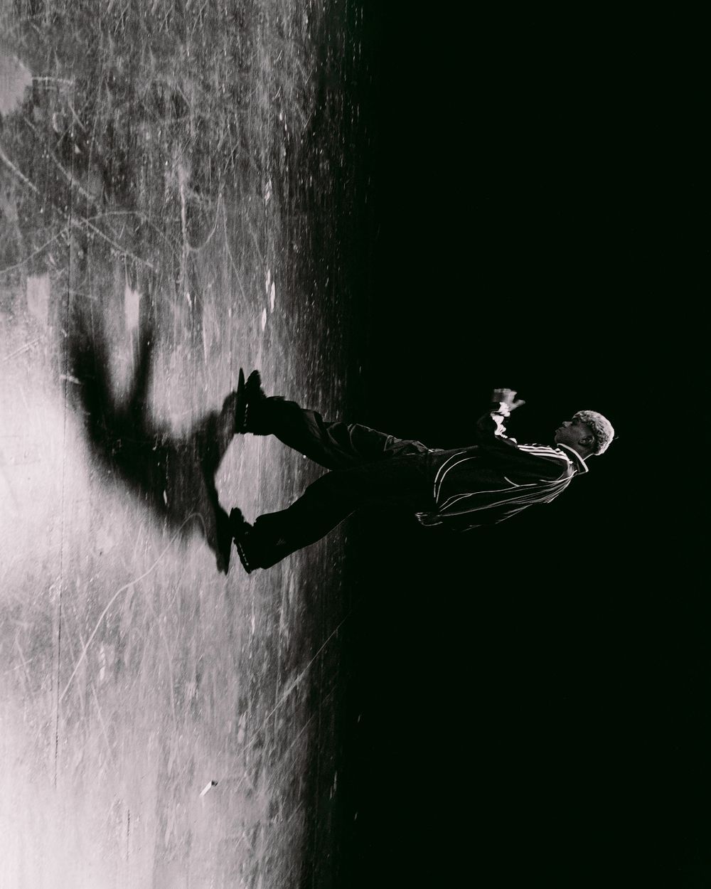 Dramatic black and white photo of a person appearing to float horizontally against a textured wall.