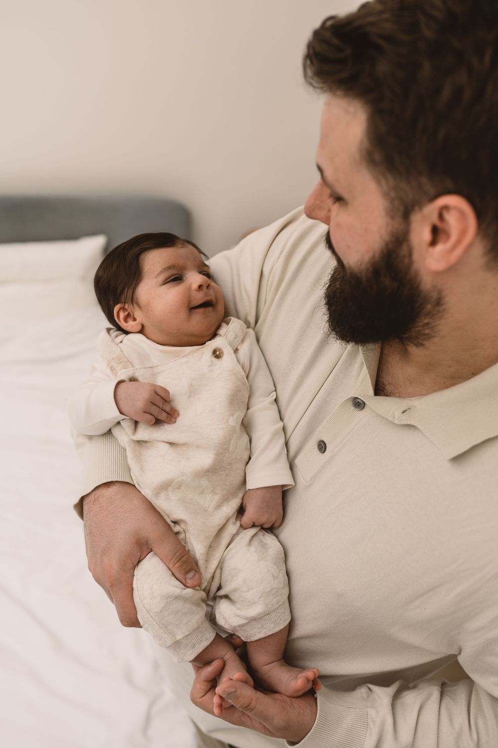 A tender moment between a father and infant on white bedding.