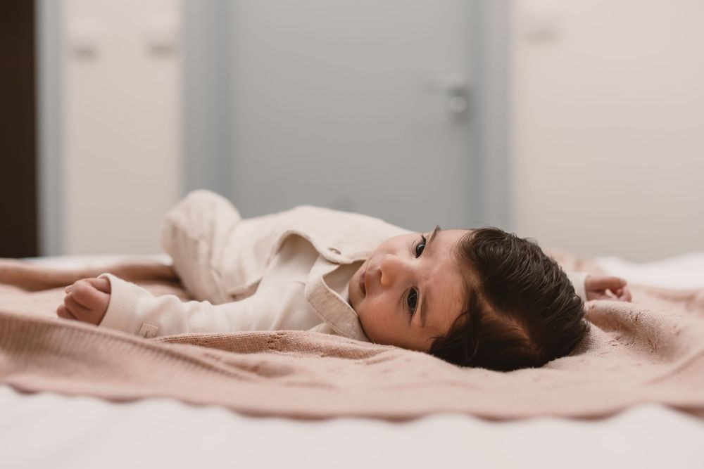 Baby lying comfortably in bed with white sheets and pillows in a bright, serene bedroom setting.